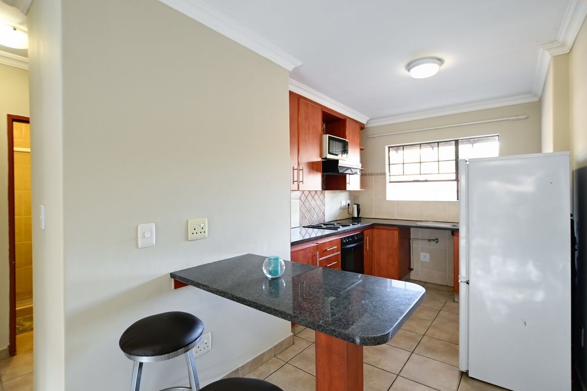 Functional kitchen featuring wooden cabinetry, granite countertops, built-in oven and hob, and an integrated breakfast bar area.