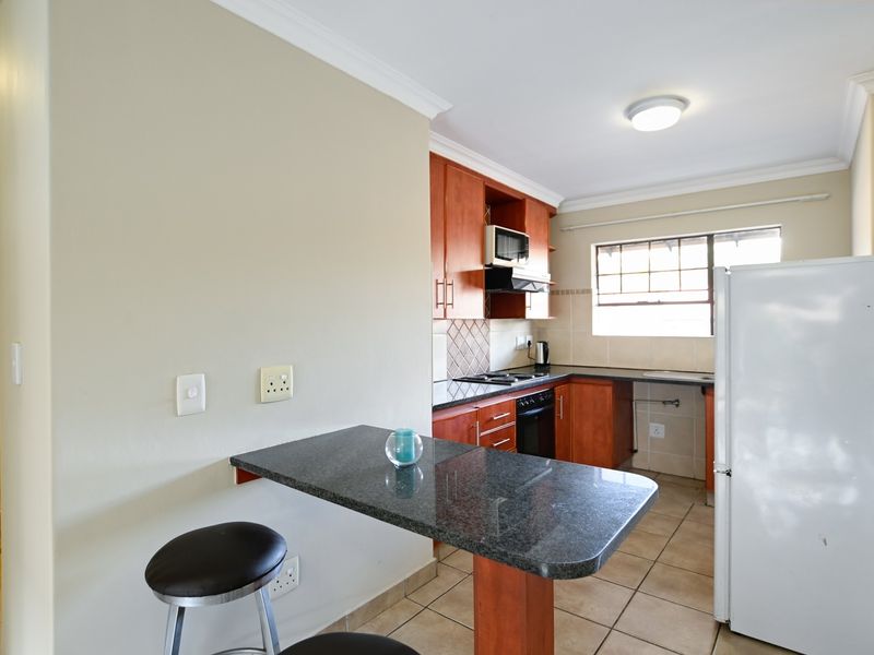 Functional kitchen featuring wooden cabinetry, granite countertops, built-in oven and hob, and an integrated breakfast bar area.