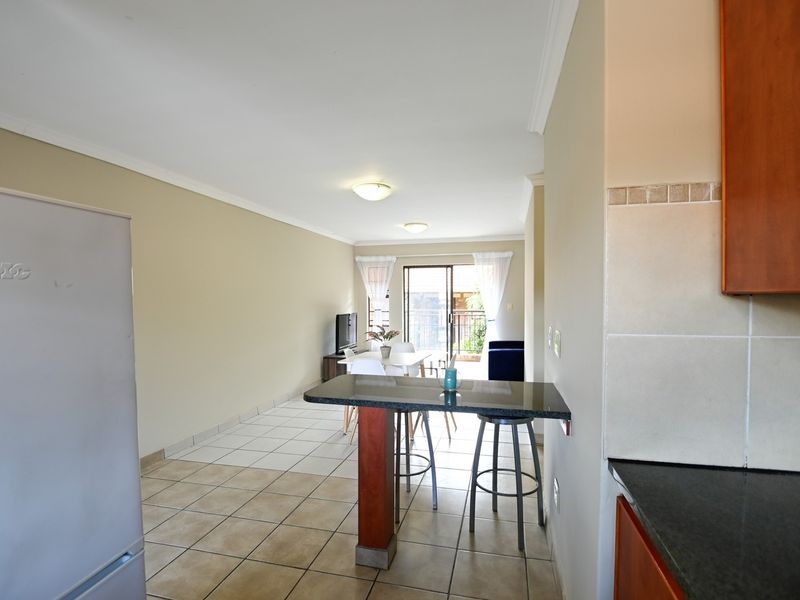 Open plan living and kitchen area featuring tiled flooring, a granite breakfast bar, and sliding door access to the balcony.