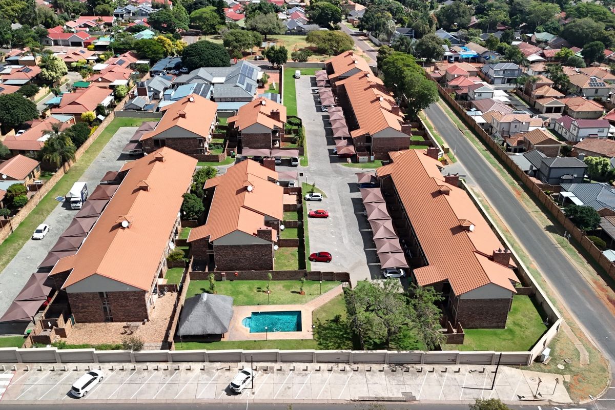 Aerial view of a residential apartment complex featuring multiple buildings with tiled roofs, a communal swimming pool, and covered parking areas.