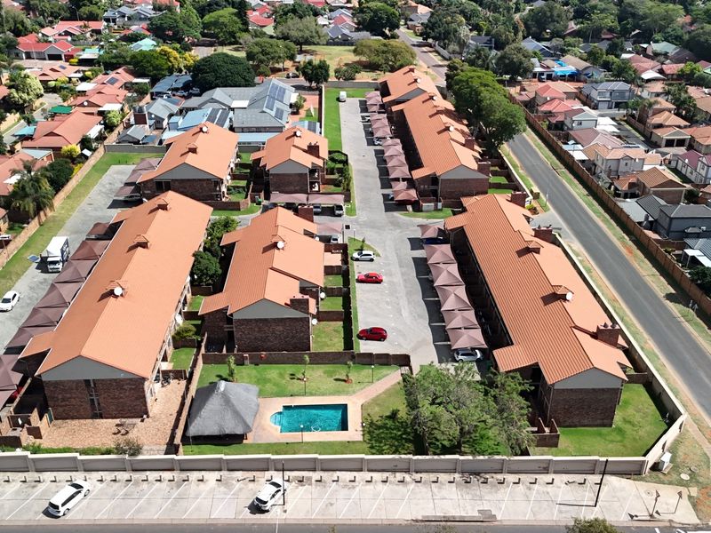 Aerial view of a residential apartment complex featuring multiple buildings with tiled roofs, a communal swimming pool, and covered parking areas.