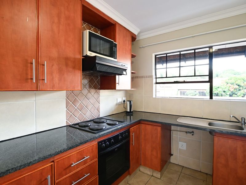 A functional kitchen featuring wooden cabinetry, granite countertops, a built-in oven with hob, and a tiled backsplash with a window view.
