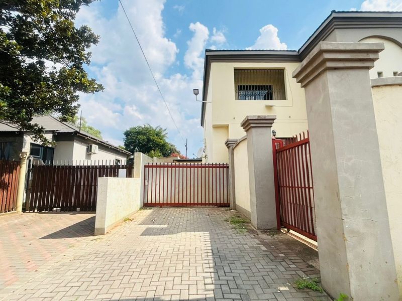 Front exterior view of the property featuring a paved driveway, secure metal gate, and perimeter walling with security features.
