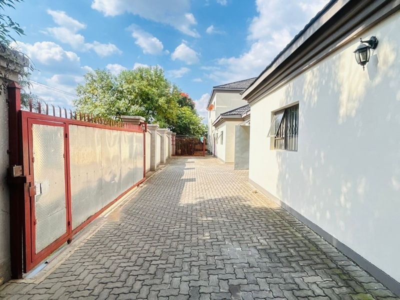 A paved driveway leading along the side of the house, featuring a secure metal gate and perimeter walling.