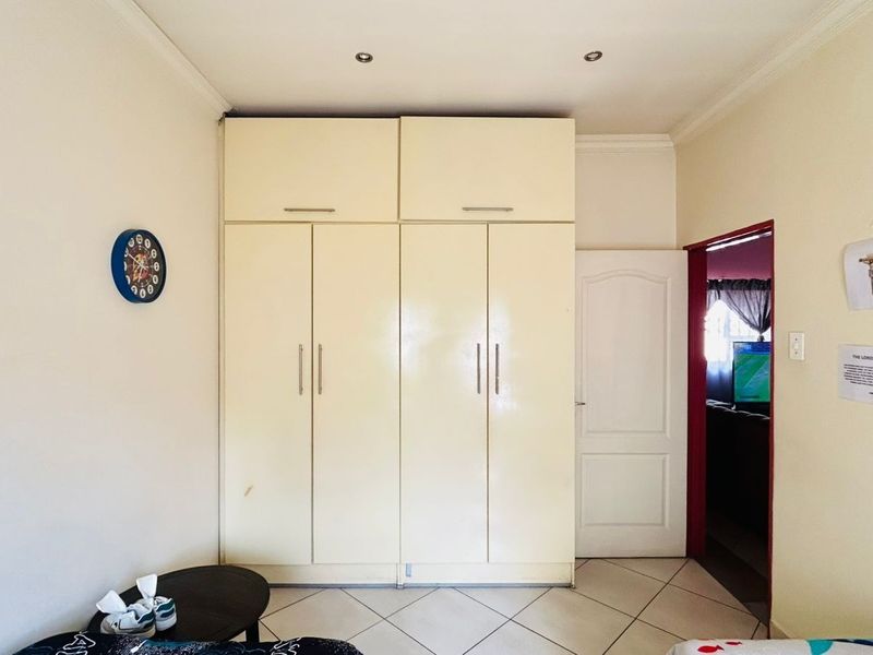 A bedroom featuring built-in cupboards with overhead storage, tiled flooring, and recessed downlighting, offering a functional and neutral living space.