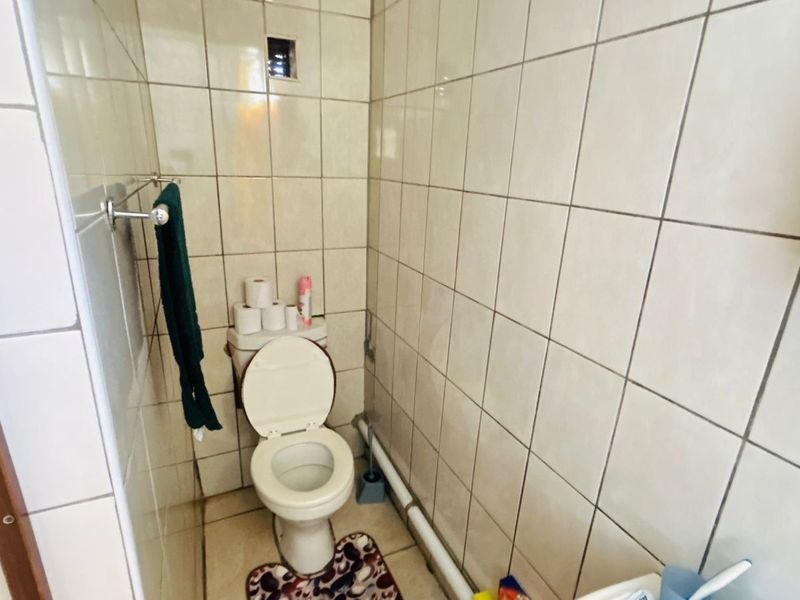 A compact bathroom featuring full-height ceramic wall tiling and a standard toilet suite, requiring cosmetic updates to improve the overall finish.