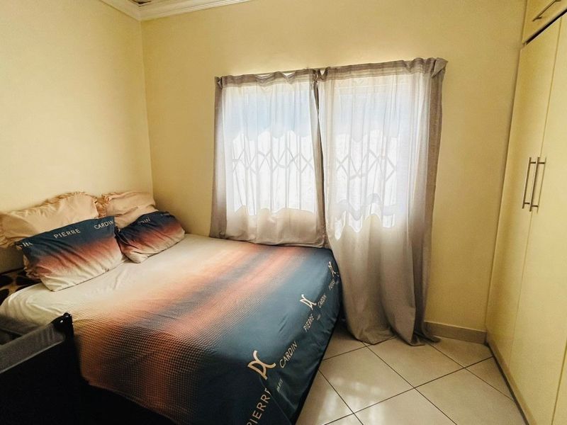 A functional bedroom featuring tiled flooring, a built-in wardrobe, and a window fitted with a security gate.