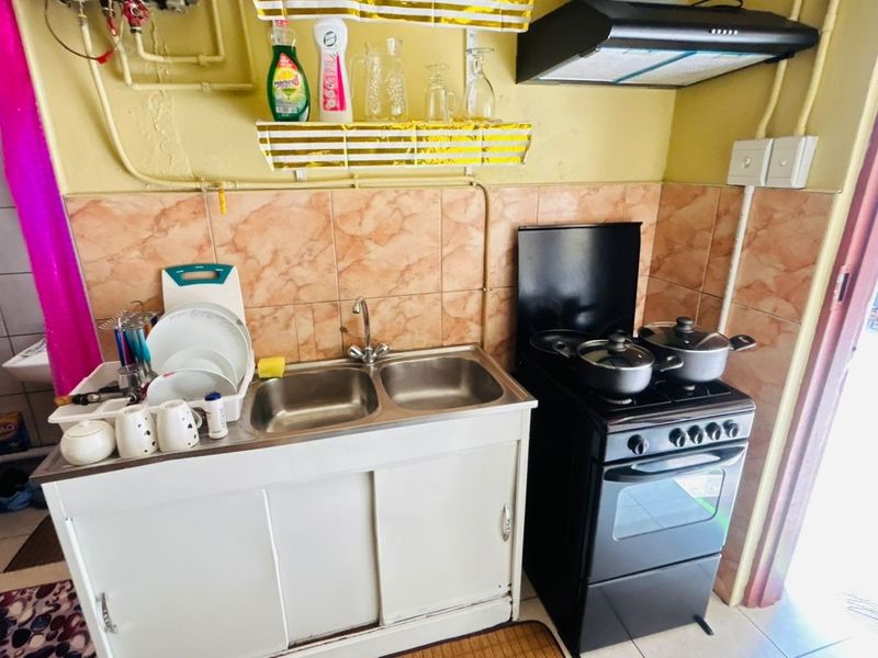 A compact kitchen area featuring a double bowl sink, tiled backsplash, and a freestanding stove with an overhead extractor fan.