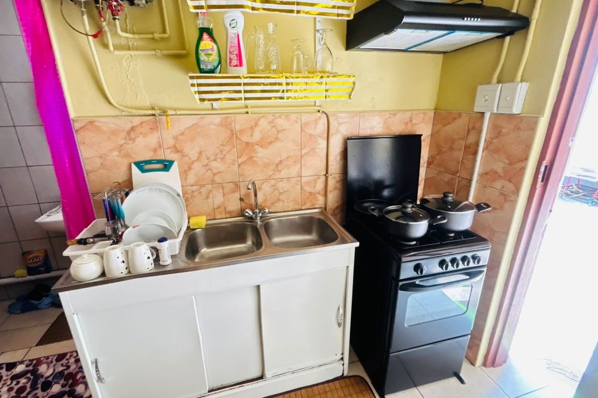 A compact kitchen area featuring a double bowl sink, tiled backsplash, and a freestanding stove with an overhead extractor fan.