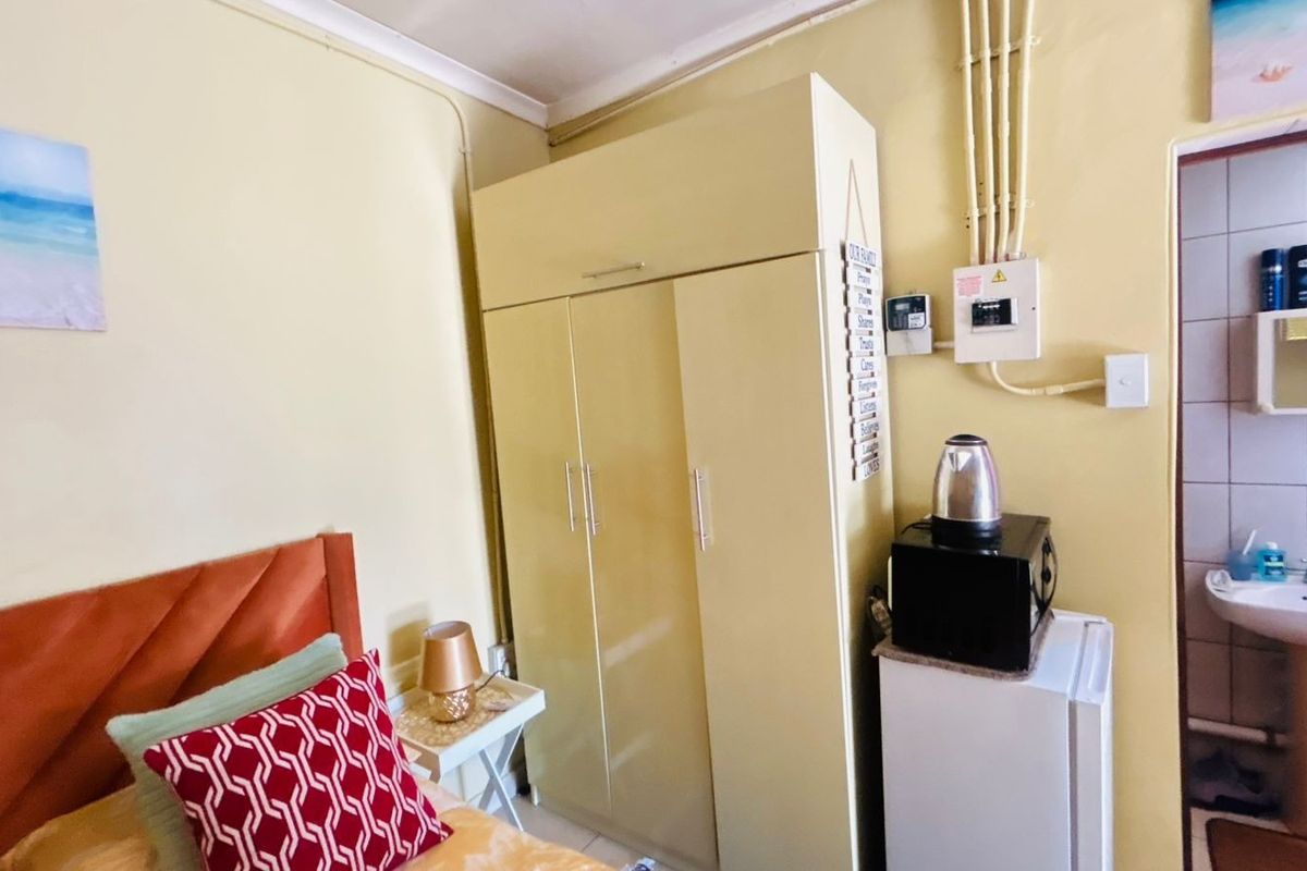A bedroom featuring a built-in wardrobe, exposed electrical conduit, and an adjacent en-suite bathroom with a pedestal basin.