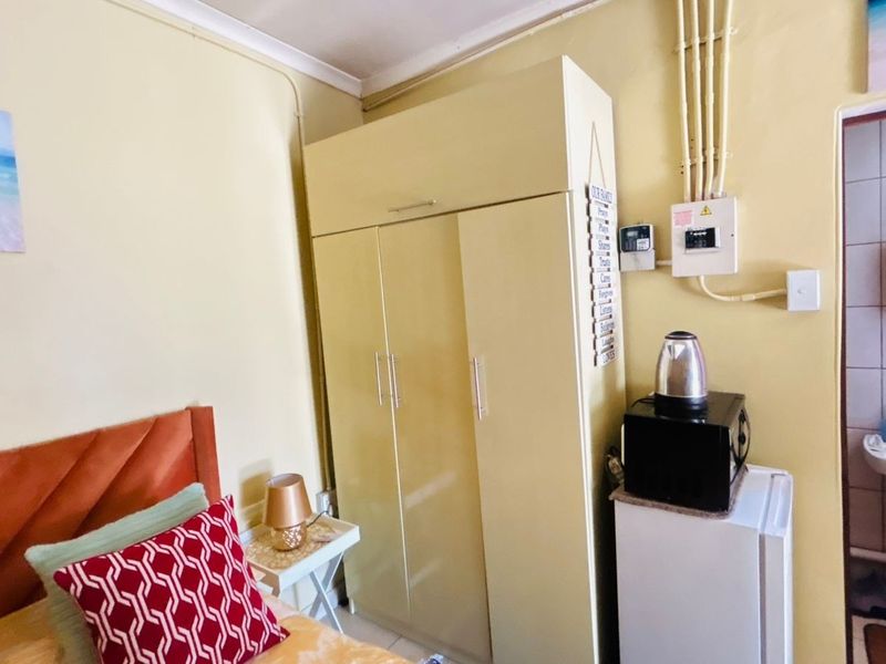 A bedroom featuring a built-in wardrobe, exposed electrical conduit, and an adjacent en-suite bathroom with a pedestal basin.