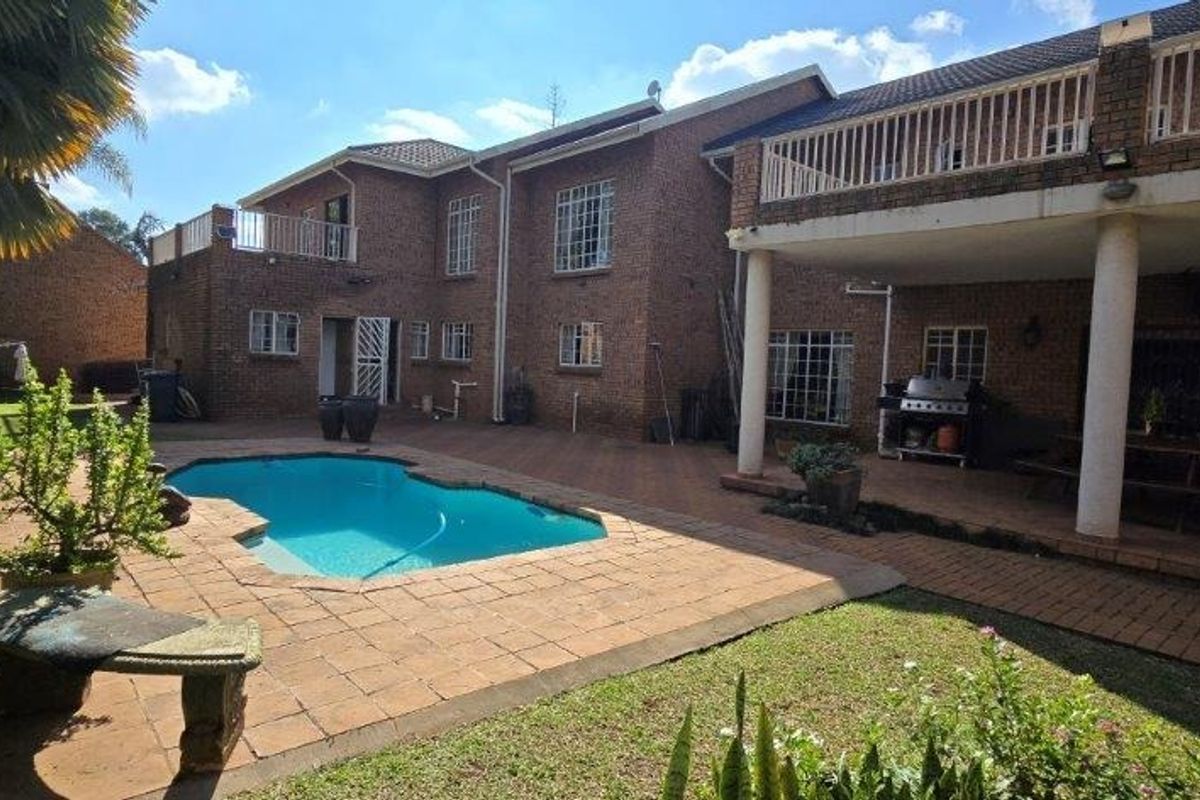 Rear view of a double-story brick house featuring a swimming pool, paved patio area, and an upper-level balcony.