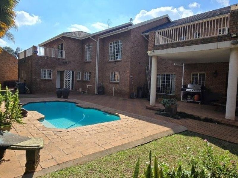 Rear view of a double-story brick house featuring a swimming pool, paved patio area, and an upper-level balcony.
