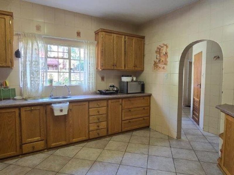 A functional kitchen featuring traditional wooden cabinetry, laminate countertops, a double sink, and tiled finishes, offering a classic layout with an arched entryway.