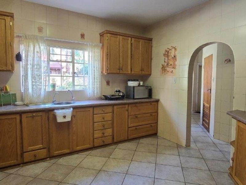 A functional kitchen featuring traditional wooden cabinetry, laminate countertops, tiled backsplash, and an arched doorway leading to the hallway.