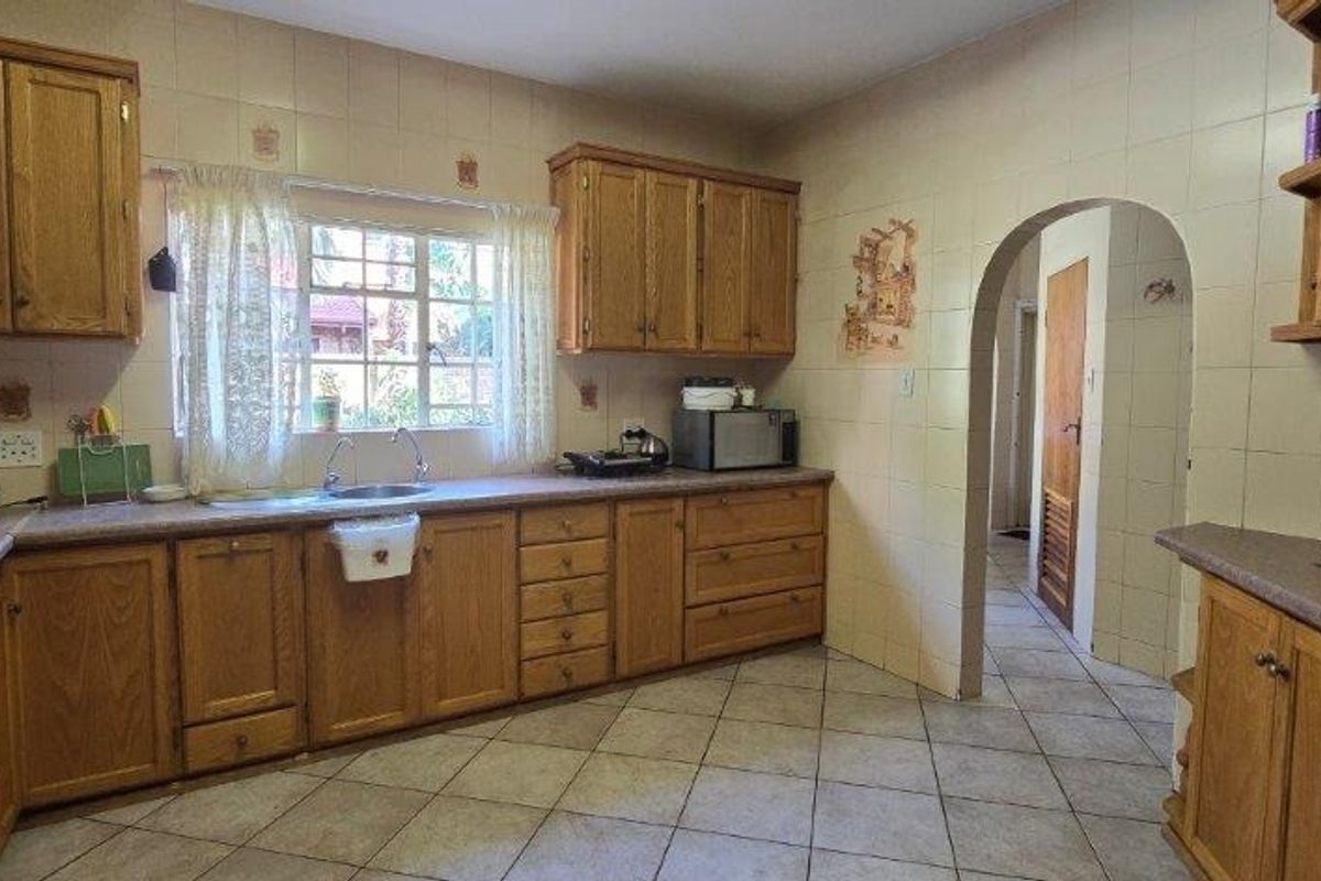 A functional kitchen featuring traditional wooden cabinetry, laminate countertops, tiled backsplash, and an arched doorway leading to the hallway.