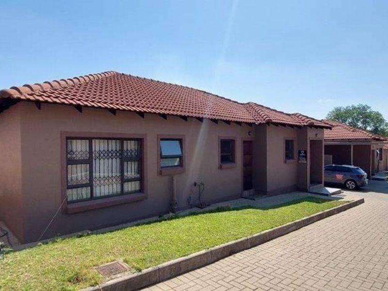 Front exterior view of a townhouse featuring a tiled roof, security bars on windows, and a paved driveway within a residential complex.