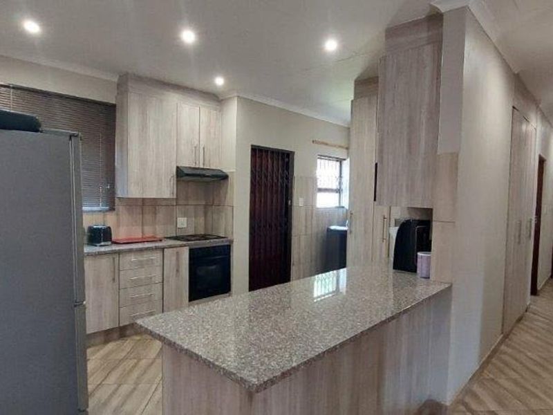 Modern kitchen featuring granite countertops, built-in cabinetry, and integrated appliances, flowing into a hallway with tiled flooring and recessed lighting.