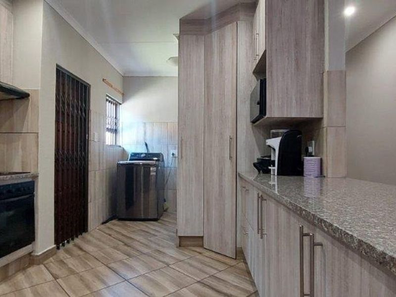 Modern kitchen featuring light wood-grain cabinetry, granite countertops, built-in oven with extractor fan, and tiled flooring with an integrated laundry area.