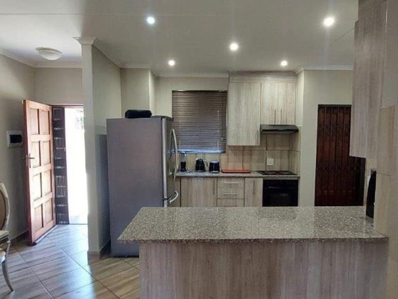 Open-plan kitchen and dining area featuring granite countertops, built-in cabinetry, and tiled flooring, with direct access to an exterior entrance.