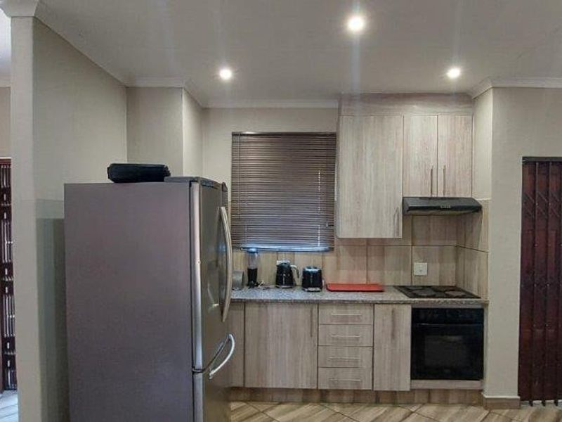 A functional kitchen featuring light wood-finish cabinetry, built-in oven and hob, extractor fan, and tiled backsplash, with direct access to an exterior security gate.