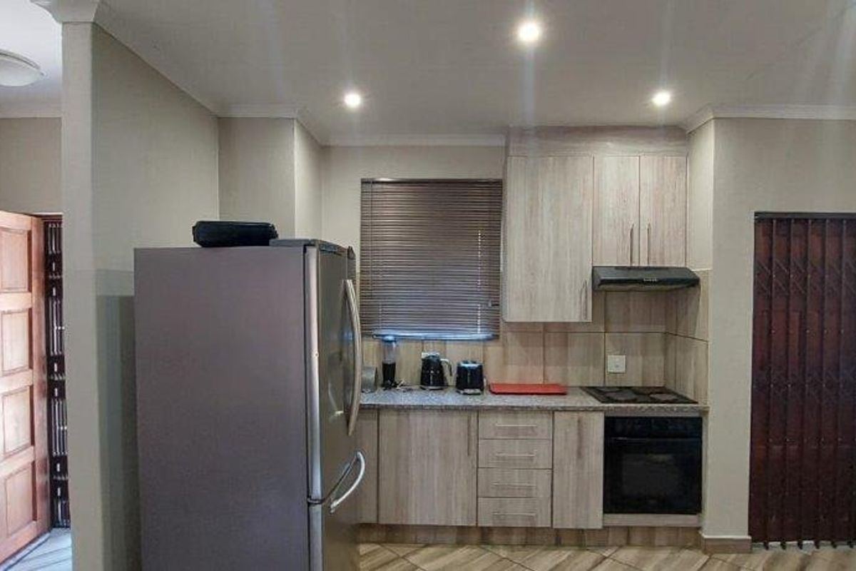 A functional kitchen featuring light wood-finish cabinetry, built-in oven and hob, extractor fan, and tiled backsplash, with direct access to an exterior security gate.