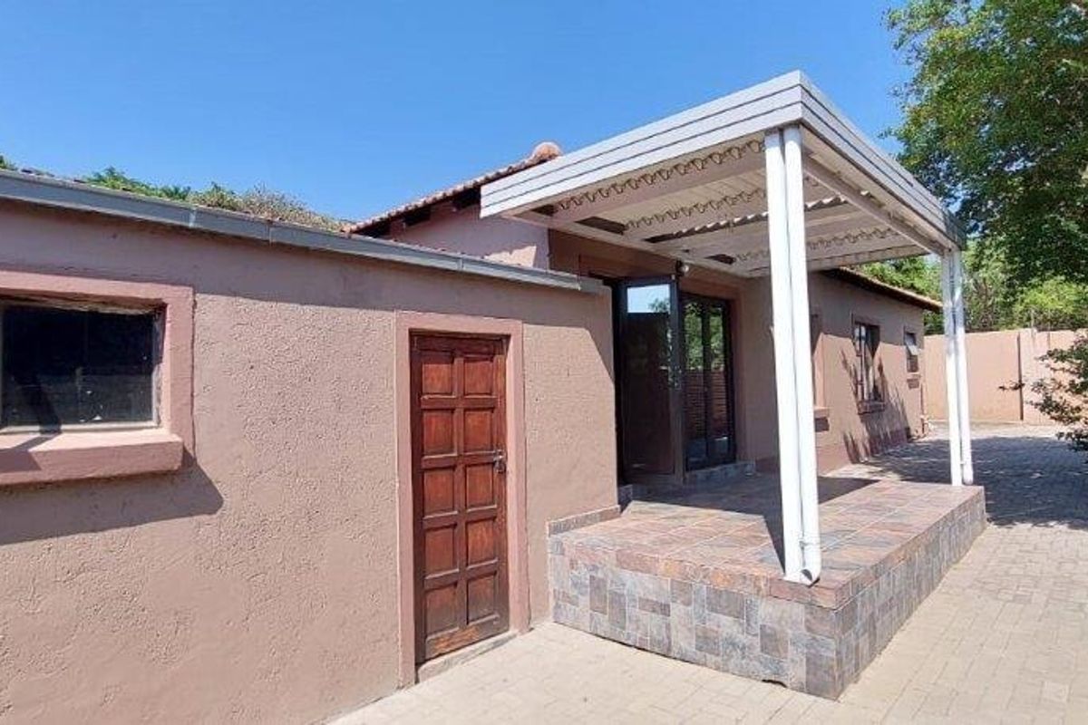 Rear exterior view of the townhouse featuring a paved courtyard, a covered patio area with a pergola, and brick boundary walls.