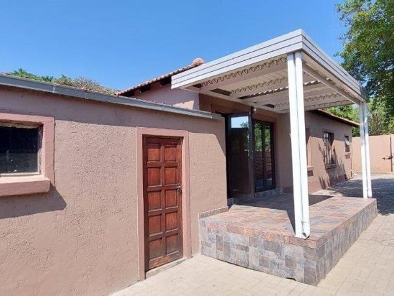 Rear exterior view of the townhouse featuring a paved courtyard, a covered patio area with a pergola, and brick boundary walls.