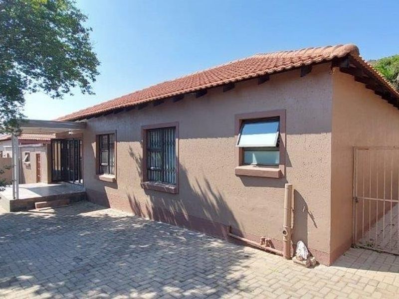 Rear exterior view of the townhouse featuring a paved courtyard, covered patio area, security gates, and terracotta tiled roof.