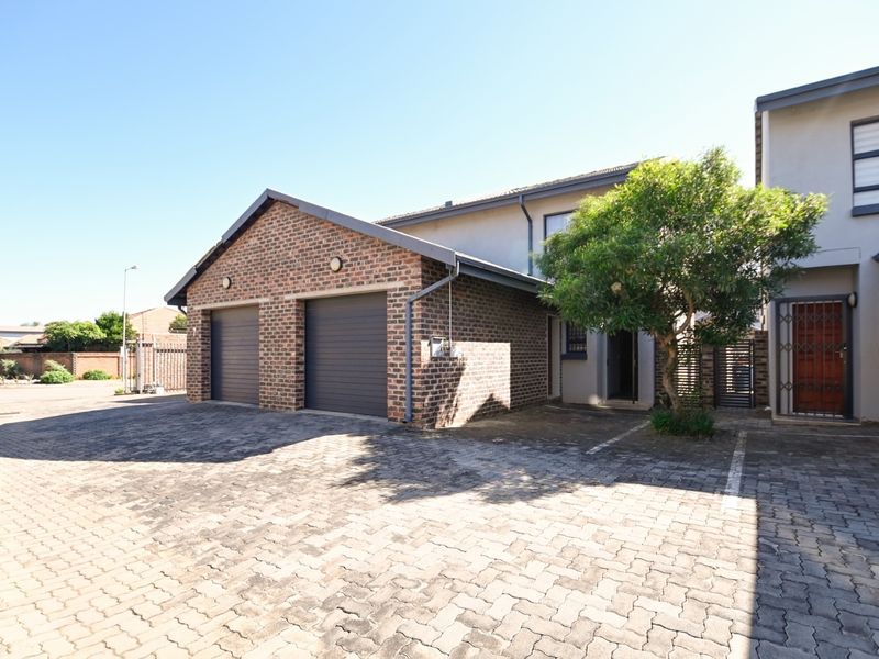 Front exterior view of the townhouse featuring a double garage, paved driveway, and secure entrance gate.