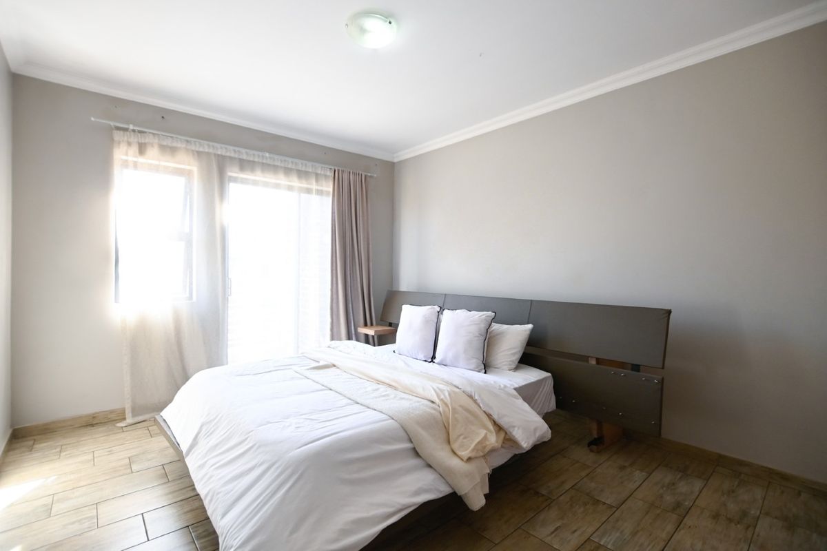 A well-lit bedroom featuring tiled flooring, coved ceilings, and a sliding glass door providing natural light.