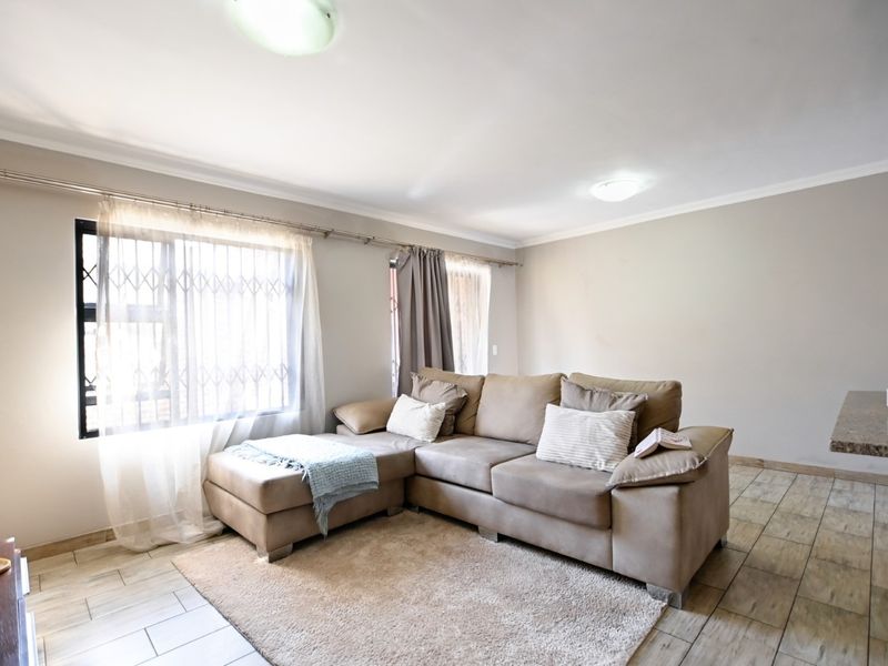 A neutrally painted living room featuring tiled flooring, large windows with security gates, and ceiling-mounted lighting, offering a functional and well-lit living space.