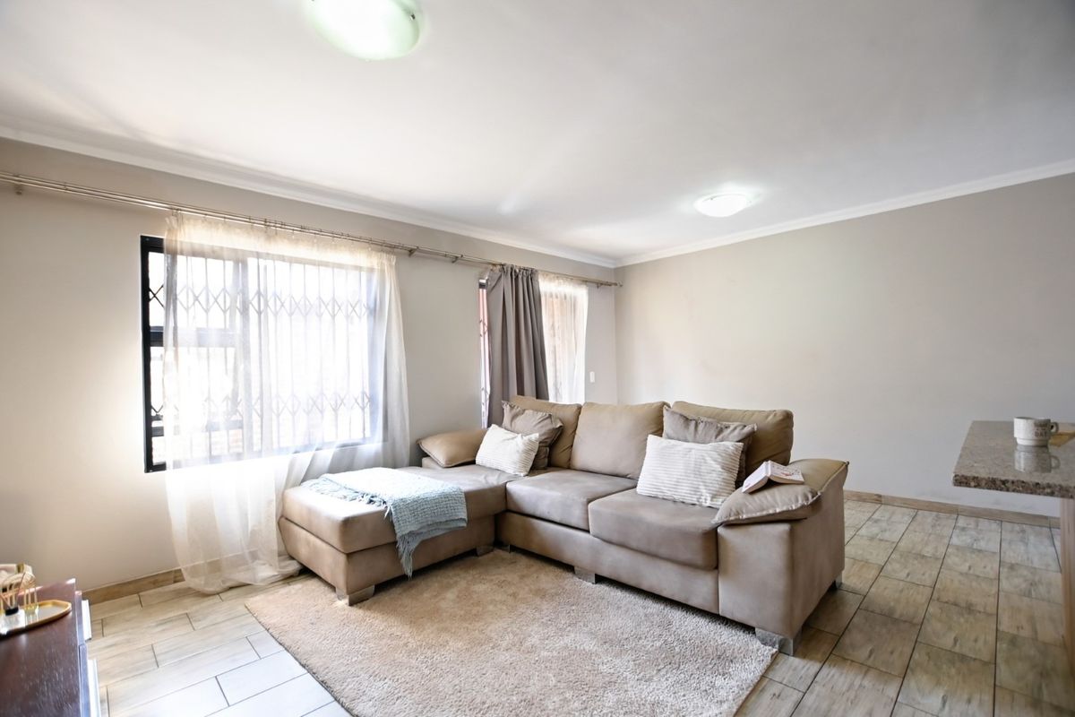 A neutrally painted living room featuring tiled flooring, large windows with security gates, and ceiling-mounted lighting, offering a functional and well-lit living space.