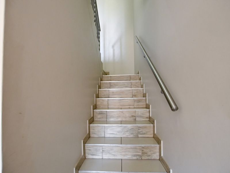 A clean, well-maintained staircase featuring wood-look ceramic tiles and a modern stainless steel handrail leading to the upper level.