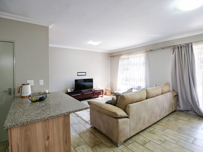 An open-plan living area featuring wood-look tile flooring, a granite breakfast bar, and large windows with security gates, creating a bright and functional space.