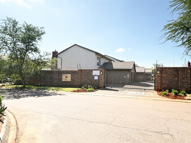 Street view of the townhouse complex entrance featuring a brick boundary wall, electric fencing, and a secure sliding gate.