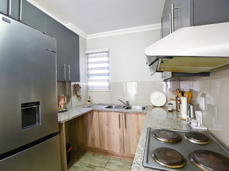 Functional kitchen featuring granite countertops, wood-finish cabinetry, stainless steel sink, and built-in electric hob with extractor fan.