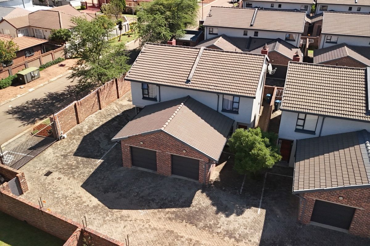 Aerial view of a townhouse complex featuring a double garage, tiled roofing, and a paved driveway within a secure perimeter-walled estate.