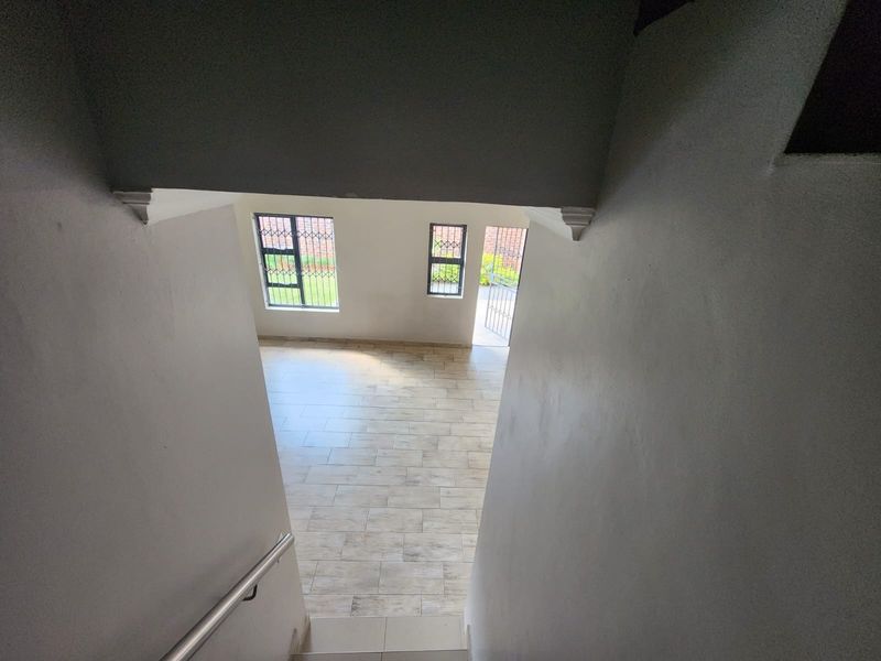 View from the staircase looking down into an open-plan living area with tiled floors, natural light, and direct access to the exterior.