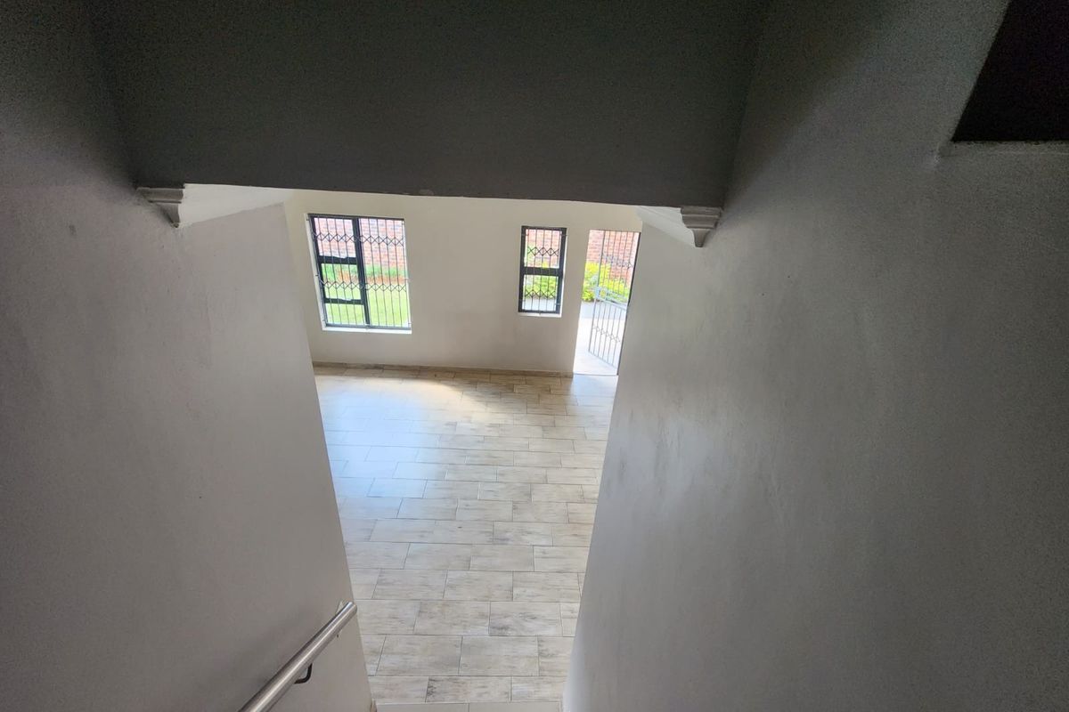 View from the staircase looking down into an open-plan living area with tiled floors, natural light, and direct access to the exterior.