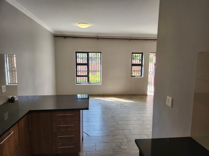 An open-plan living and kitchen area featuring tiled flooring, modern dark cabinetry with granite countertops, and security bars on the windows.