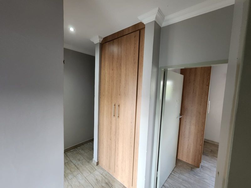 A clean, modern hallway featuring wood-finish built-in cupboards, tiled flooring, and decorative crown molding, providing efficient storage and a bright, neutral aesthetic.