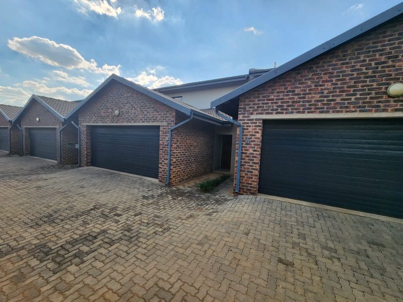 Front elevation of a townhouse complex featuring multiple garages with dark sectional doors and a paved driveway.