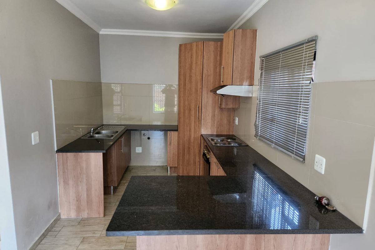 A functional kitchen featuring laminate cabinetry, granite countertops, a built-in hob with extractor fan, and a double sink with tiled splashbacks.