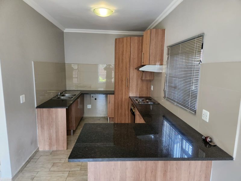 A functional kitchen featuring laminate cabinetry, granite countertops, a built-in hob with extractor fan, and a double sink with tiled splashbacks.