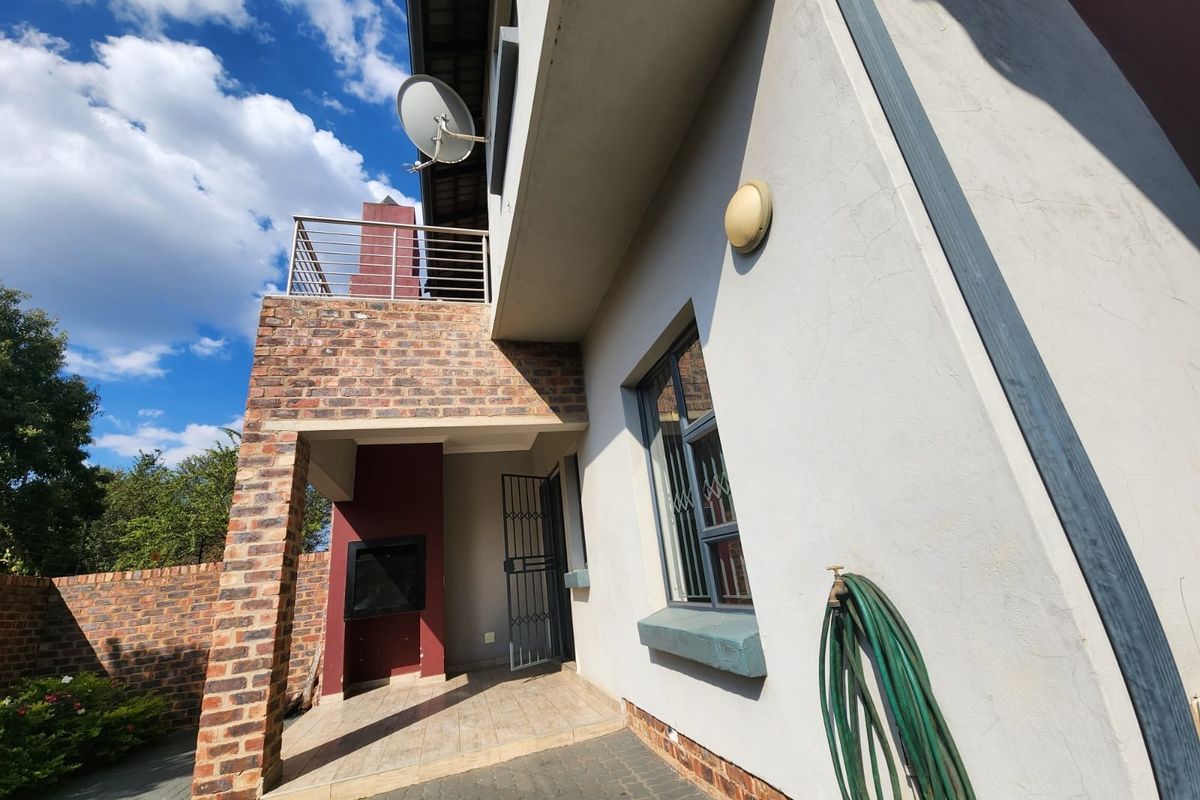 Rear exterior view of the townhouse featuring a paved patio area with a built-in braai and an upper-level balcony with metal railings.