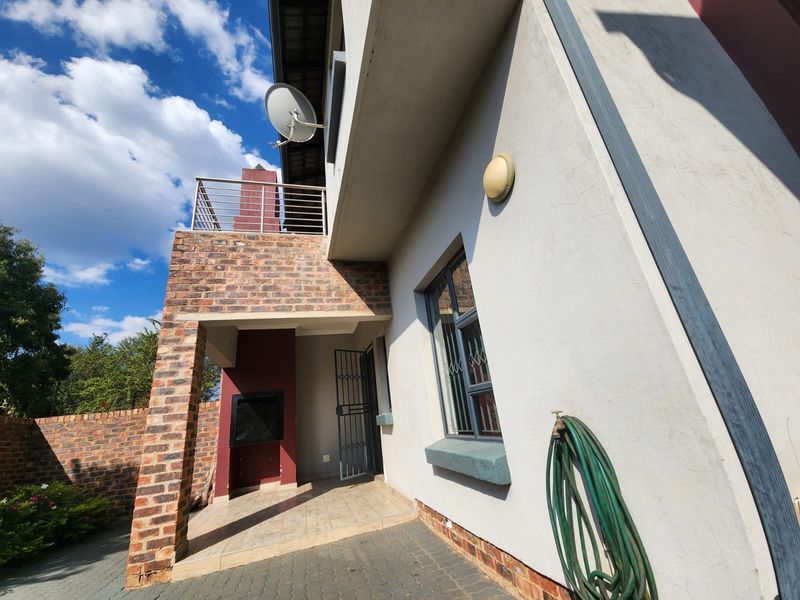 Rear exterior view of the townhouse featuring a paved patio area with a built-in braai and an upper-level balcony with metal railings.