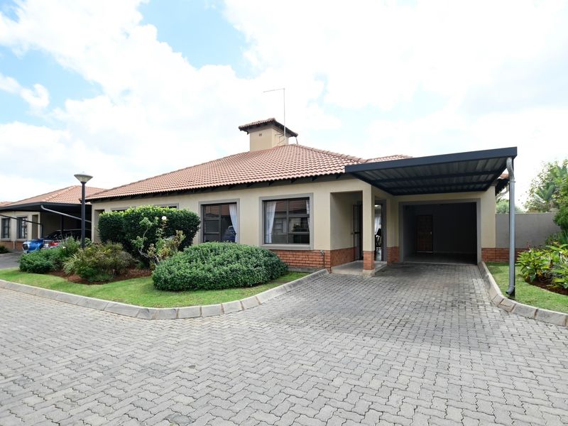 Front view of a townhouse featuring a tiled roof, brick accents, a paved driveway, and a covered carport area.