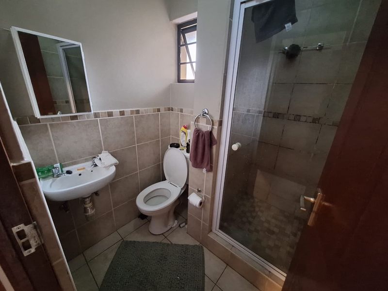 A functional bathroom featuring a shower enclosure, wall-mounted basin, and toilet with neutral tiled finishes.