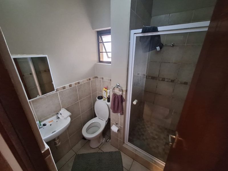A compact bathroom featuring a shower enclosure, wall-mounted basin, and toilet with neutral tiled finishes.